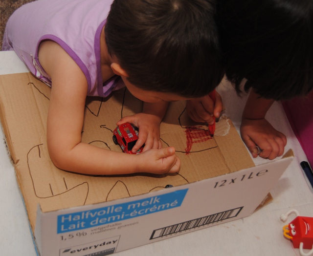 Kind tekent een speelstad op een kartonnen doos